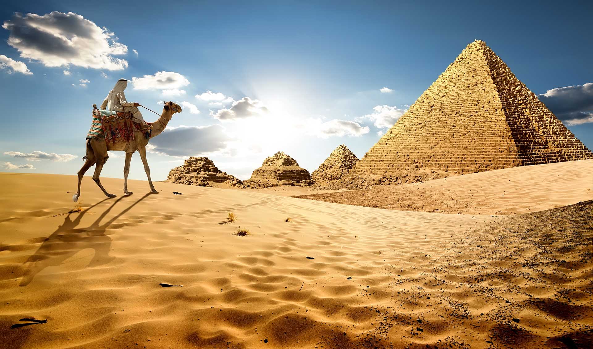 Bedouin on camel near pyramids in desert